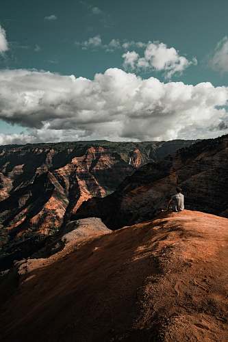 waimea canyon person sitting on mountain cliff grey